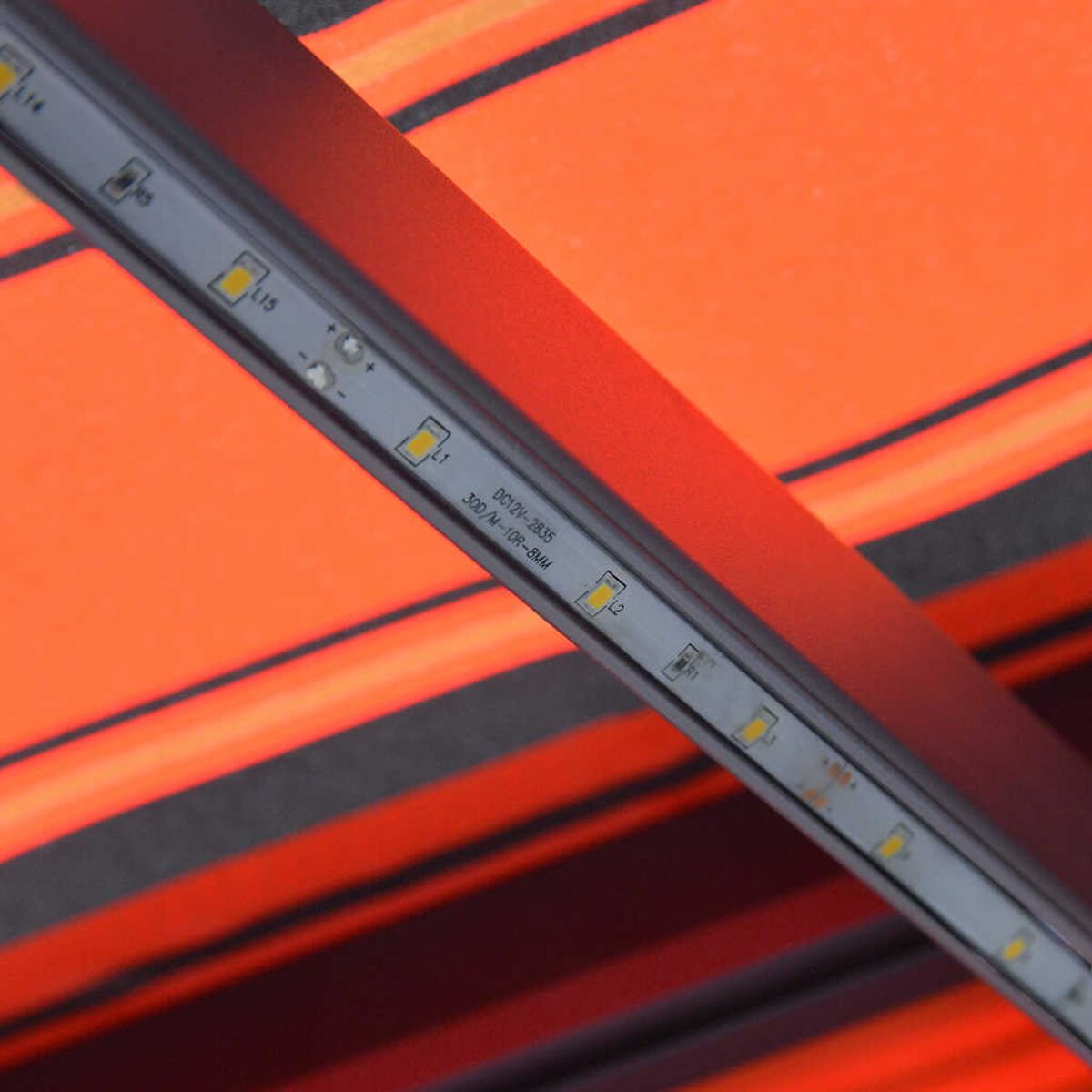 Nahaufnahme eines orange-schwarz gestreiften Markisendachs mit LED-Lichtleiste.