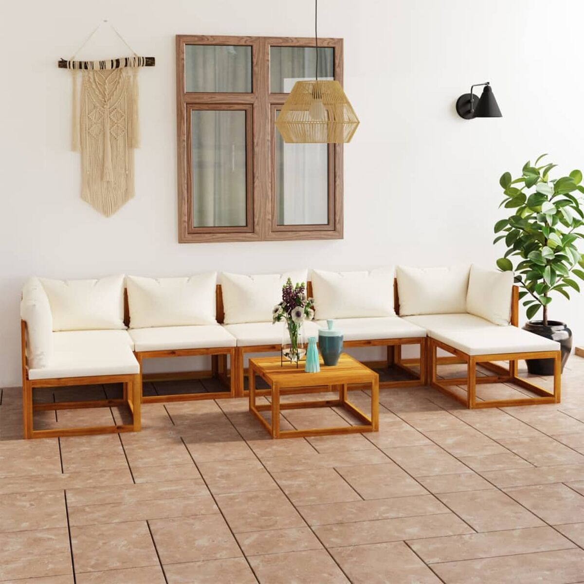 Sitzbereich im Freien mit weißen Kissen. Enthält einen Tisch, einen Teppich und Pflanzen. Hintergrund ist ein Haus.