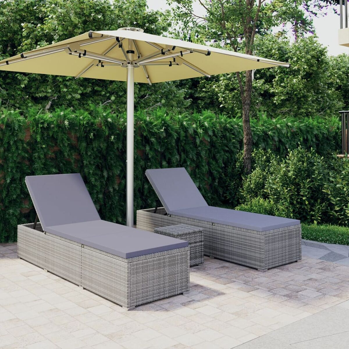 Szene im Freien mit grauen Sonnenliegen, Tisch und Sonnenschirm vor grünem Laub.