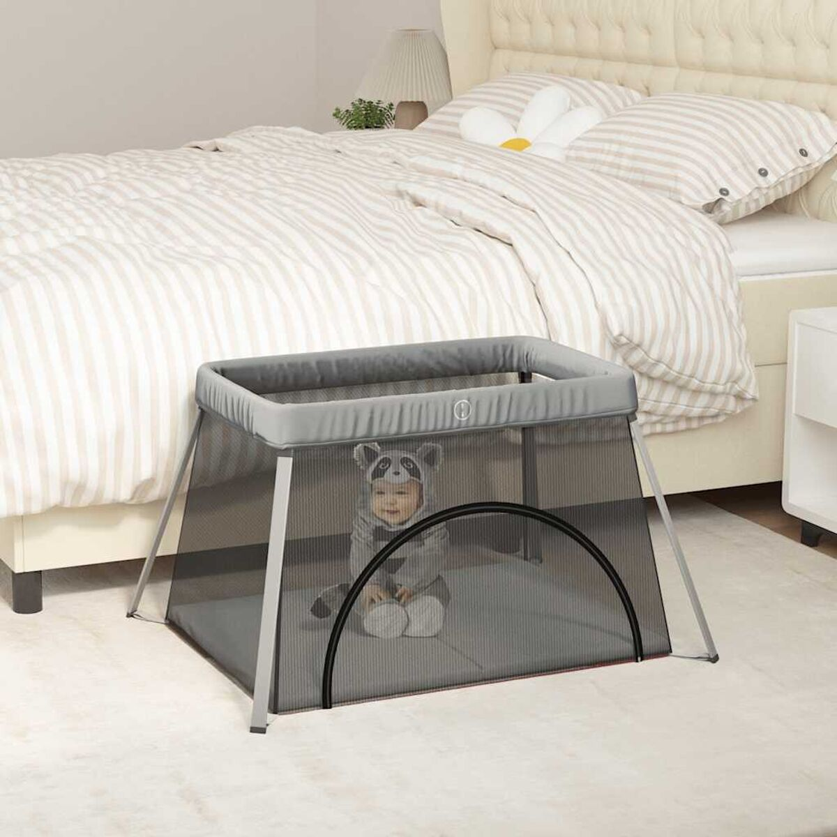 Baby in einem Laufstall in einem Zimmer. Der Laufstall ist grau und transparent.