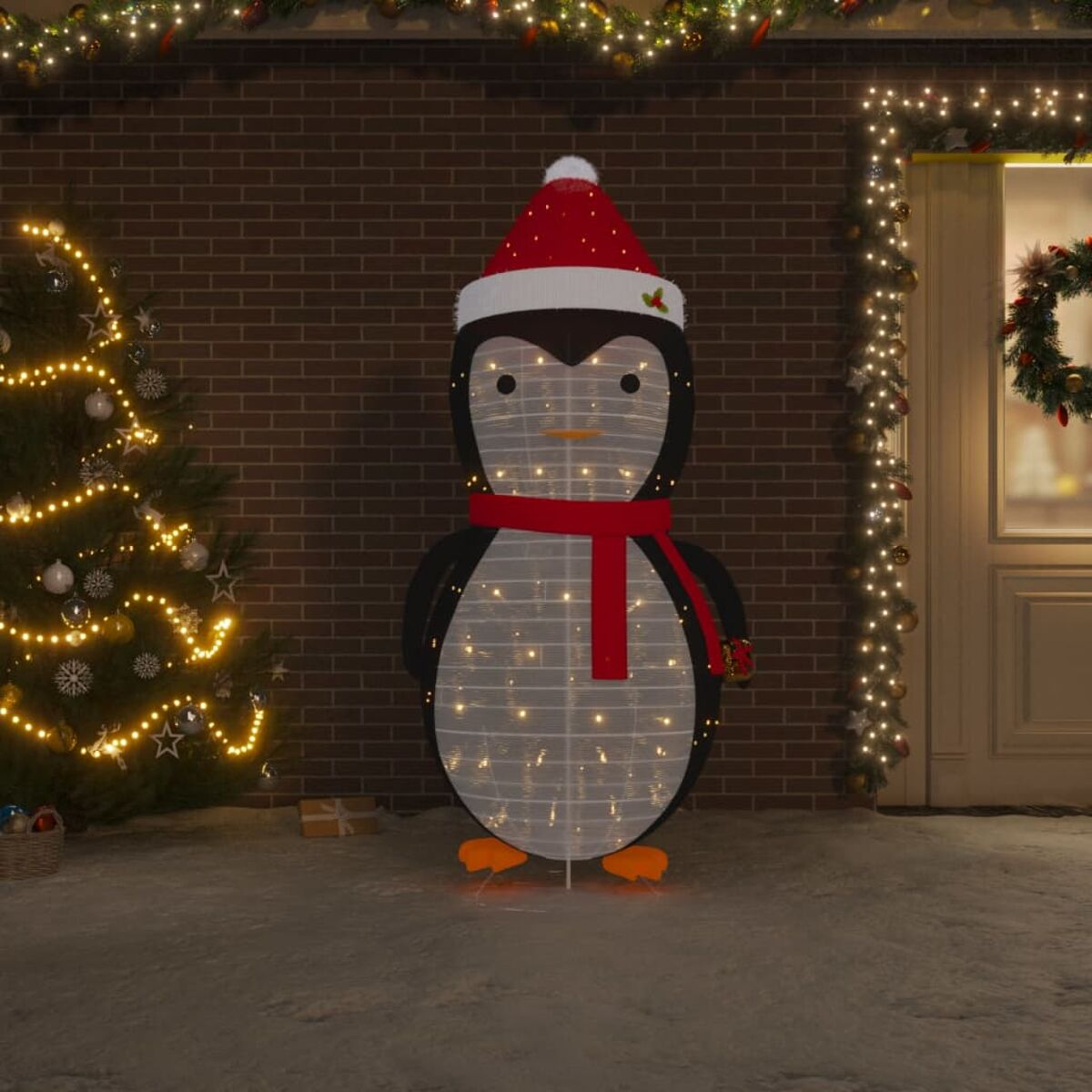 Pinguin-Weihnachtsdekoration, beleuchtet, mit Hut und Schal. Ziegelwandhintergrund.