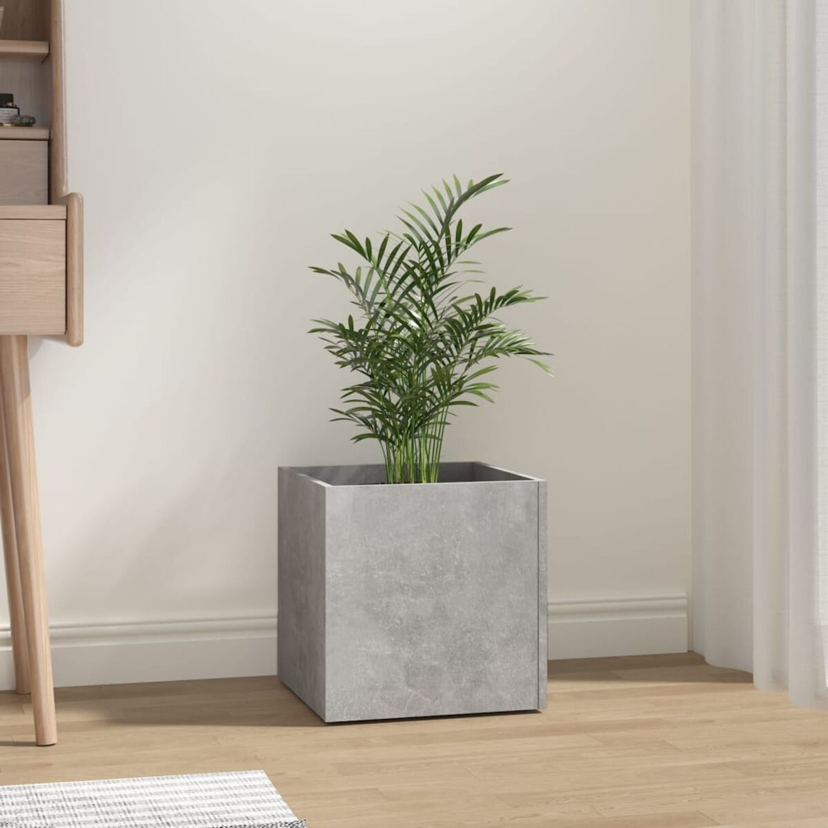 Ein quadratischer grauer Betonpflanzer mit einer kleinen grünen Pflanze darin, auf einem Holzboden.