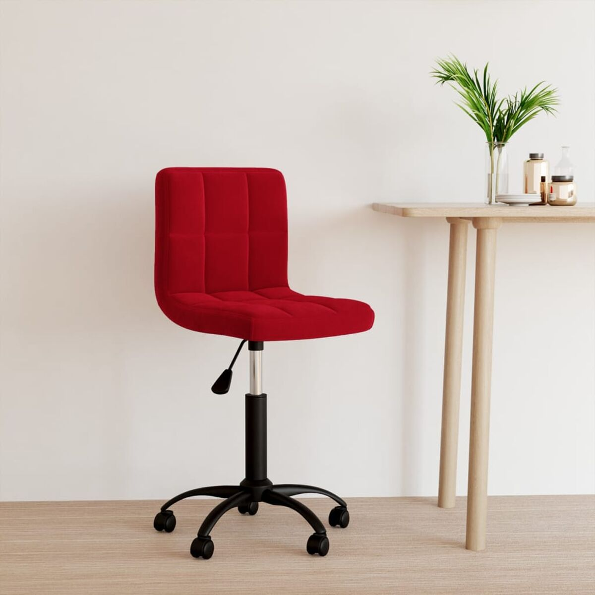 Roter Bürostuhl mit schwarzem Gestell und Rollen. Tisch und Grünzeug im Hintergrund.