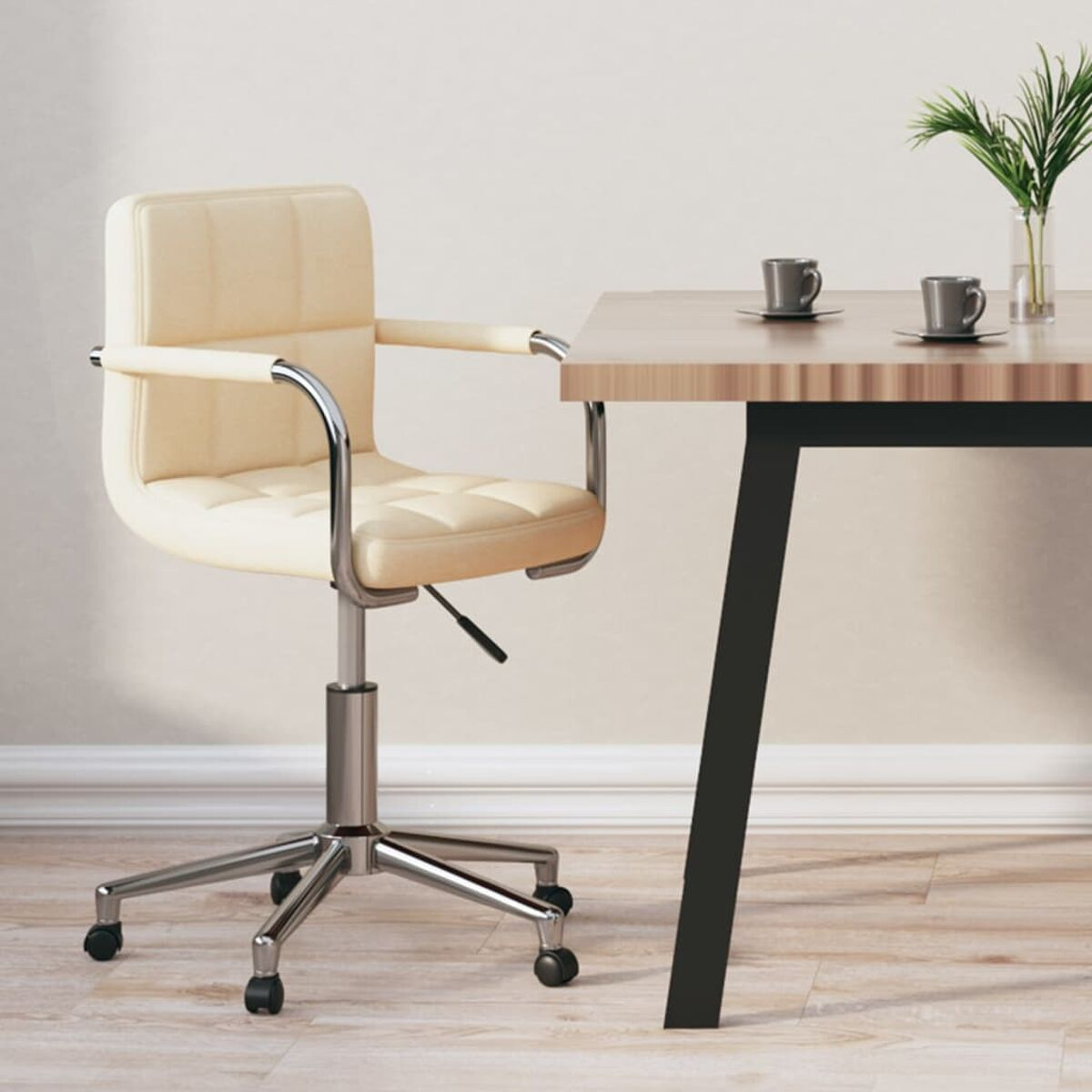 Ein Bürostuhl mit cremefarbenem Sitz und Chromfuß neben einem Holztisch mit zwei Tassen.