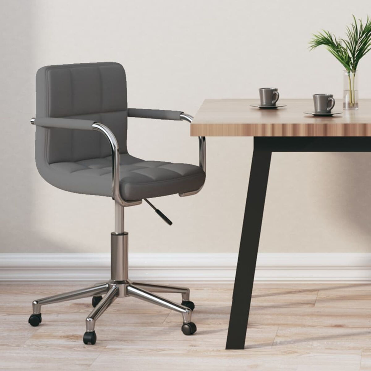 Silla de oficina gris, escritorio con tazas y una planta. Pared clara y suelo de madera.