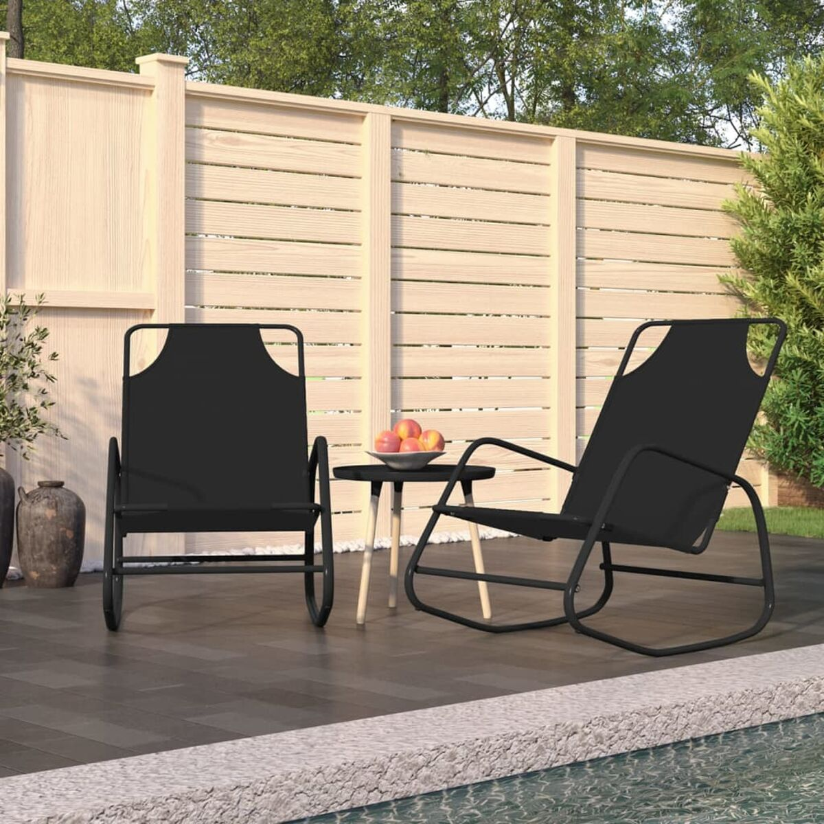 Zwei schwarze Gartenstühle und ein kleiner Tisch mit Obst auf einer Terrasse, am Pool.