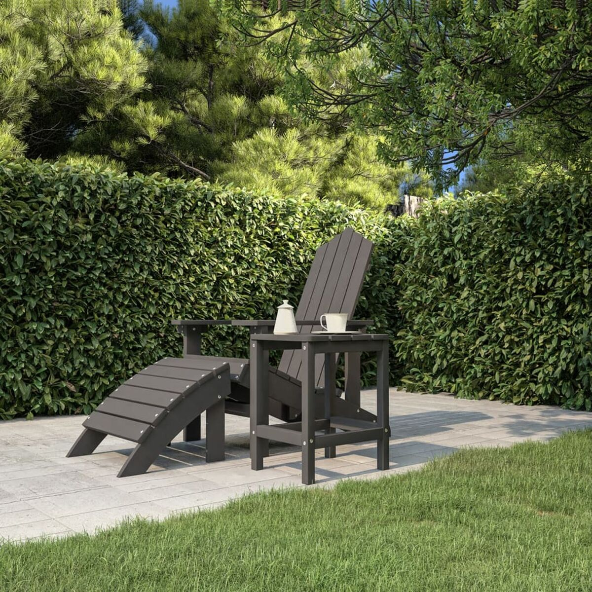 Grauer Stuhl und Fußstütze im Freien mit kleinem Tisch. Auf einer Terrasse mit grünem Hintergrund.