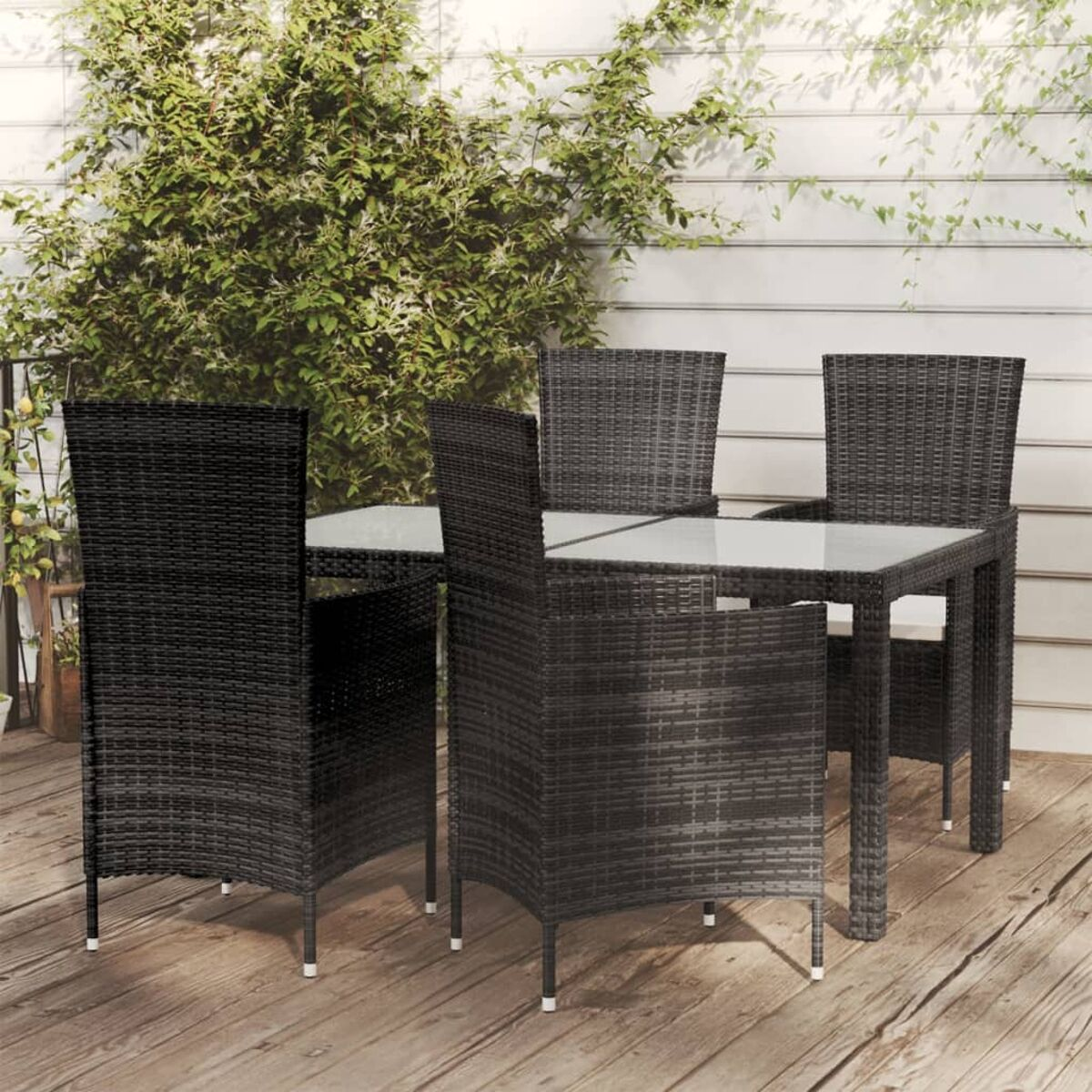 Schwarzer Korbtisch und Stühle auf einer Holzterrasse. Die Stühle haben weiße Kissen.