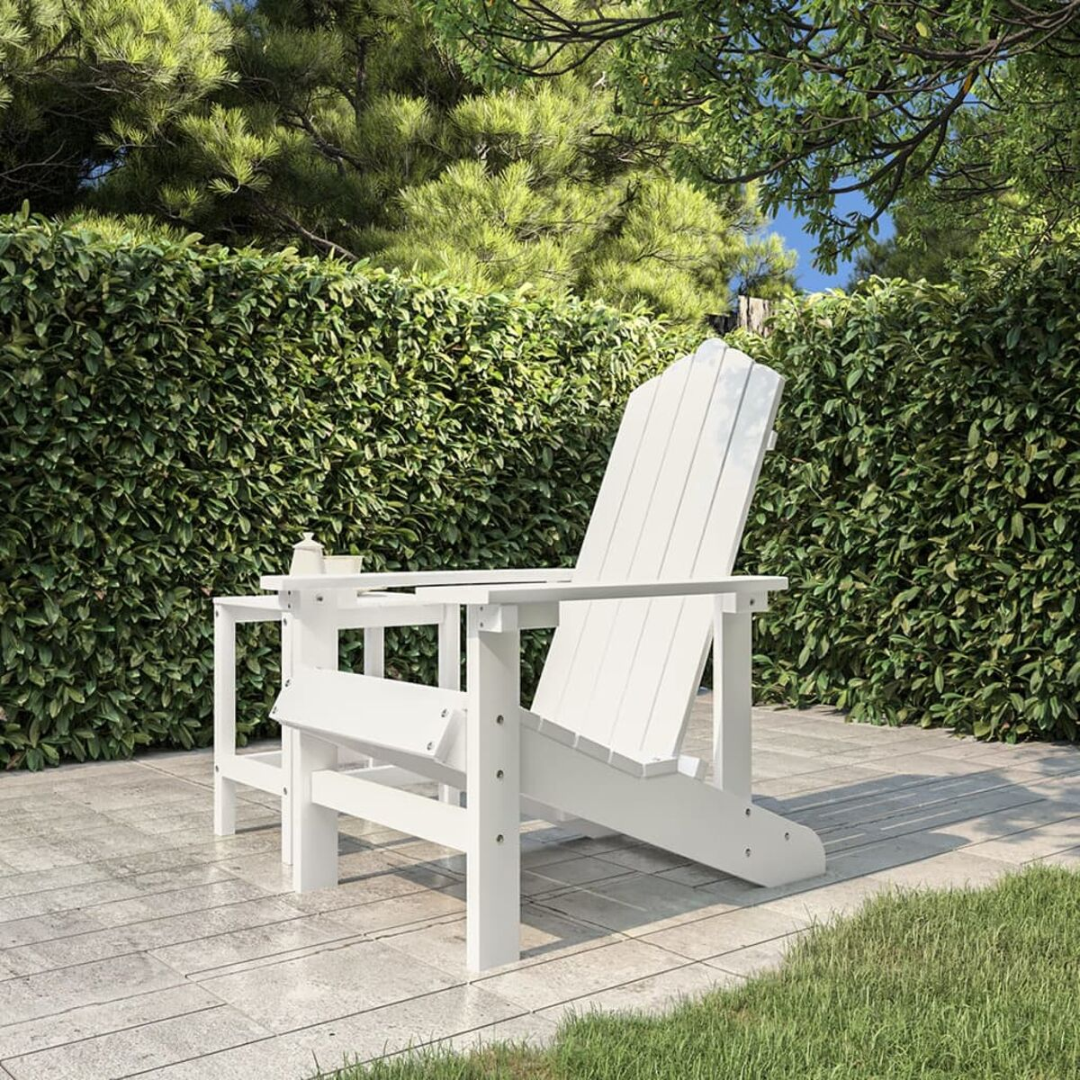 Weißer Adirondack-Stuhl auf einer Terrasse. Grüne Büsche und Gras im Hintergrund.