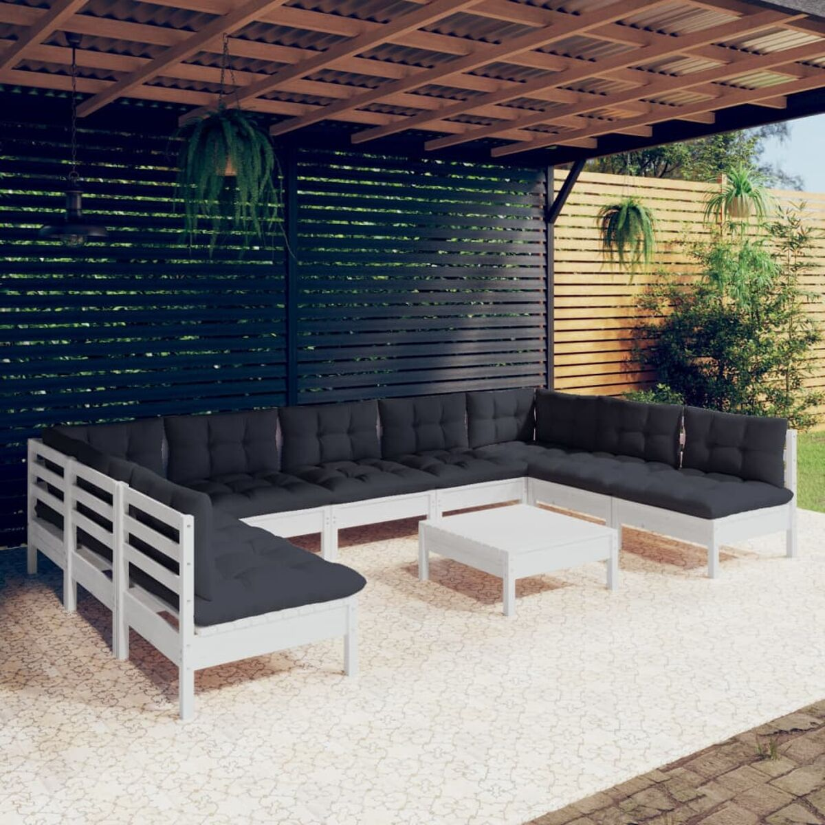 Weißes Ecksofa im Freien mit schwarzen Kissen unter einer Holzpergola. Ein kleiner Tisch ist vorhanden.