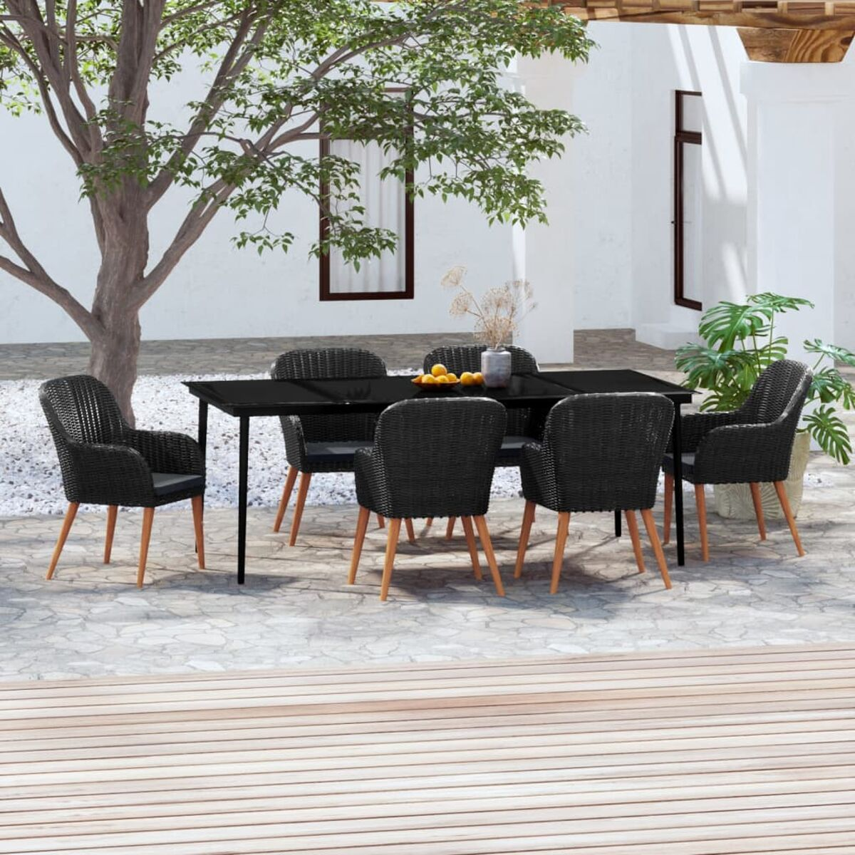Schwarzer Tisch und Stühle auf Steinterrasse. Weiße Wand und Baum im Hintergrund.