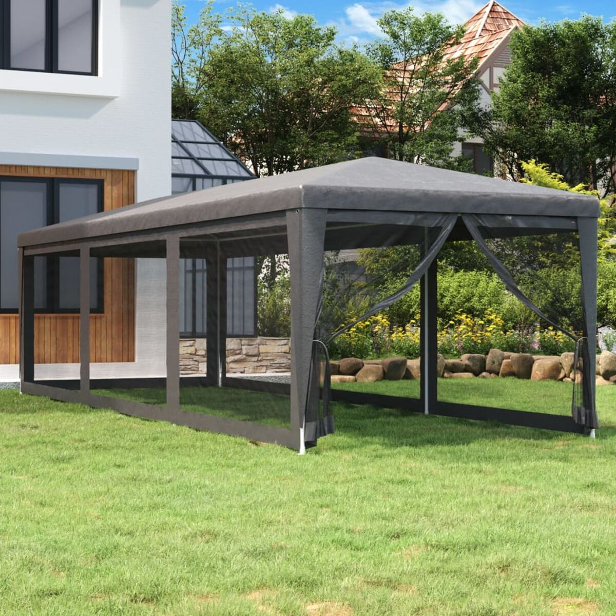 Gazebo grigio con lati in rete su erba verde, casa bianca e alberi sullo sfondo.