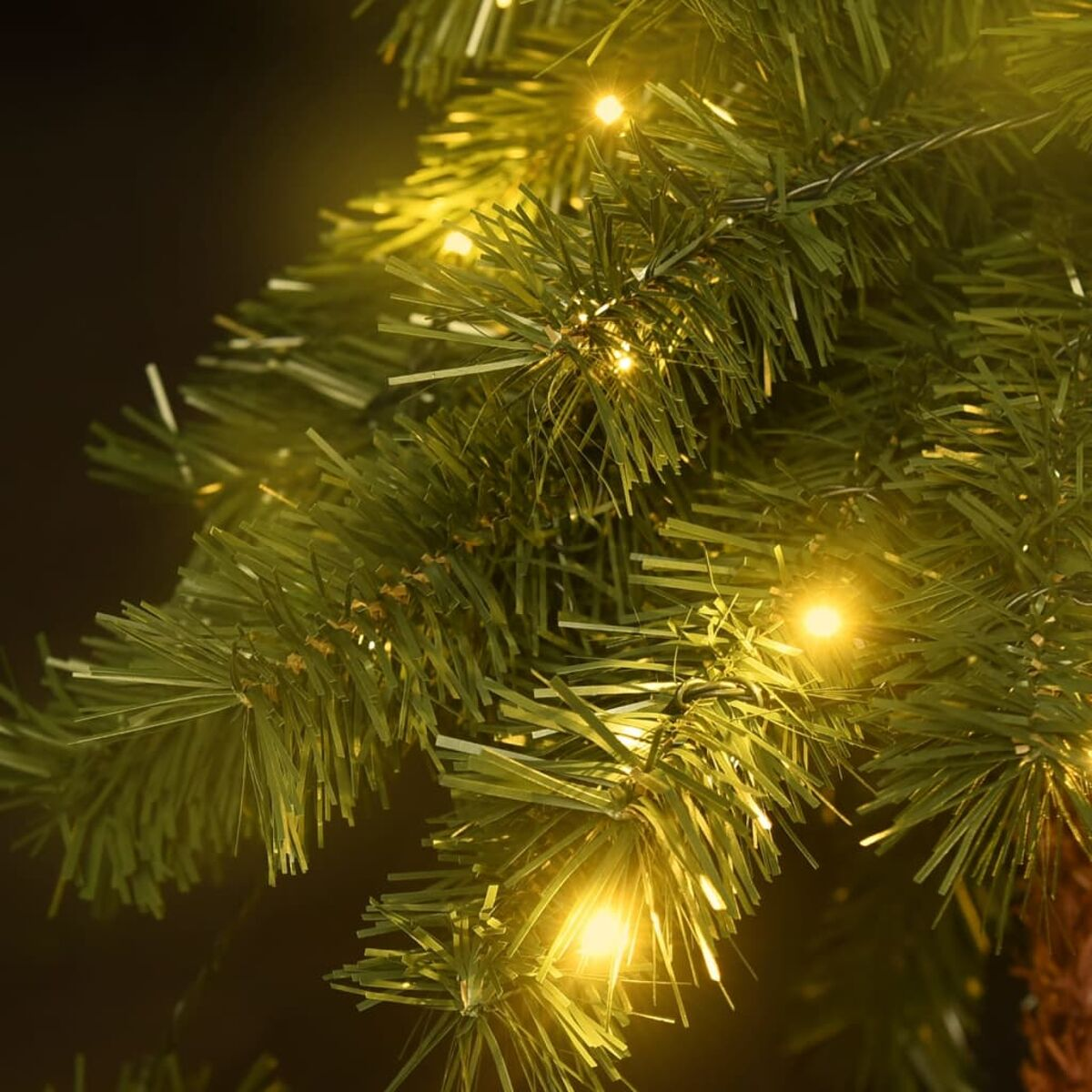 Nahaufnahme von künstlichen Weihnachtsbaumzweigen mit warmweißen Lichtern. Dunkler Hintergrund.