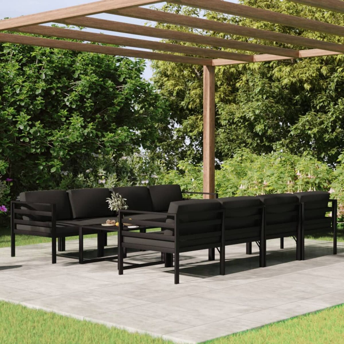 Schwarzer Sitzbereich im Freien unter einer Holzpergola. Enthält einen Tisch, Sofas und Grün im Hintergrund.