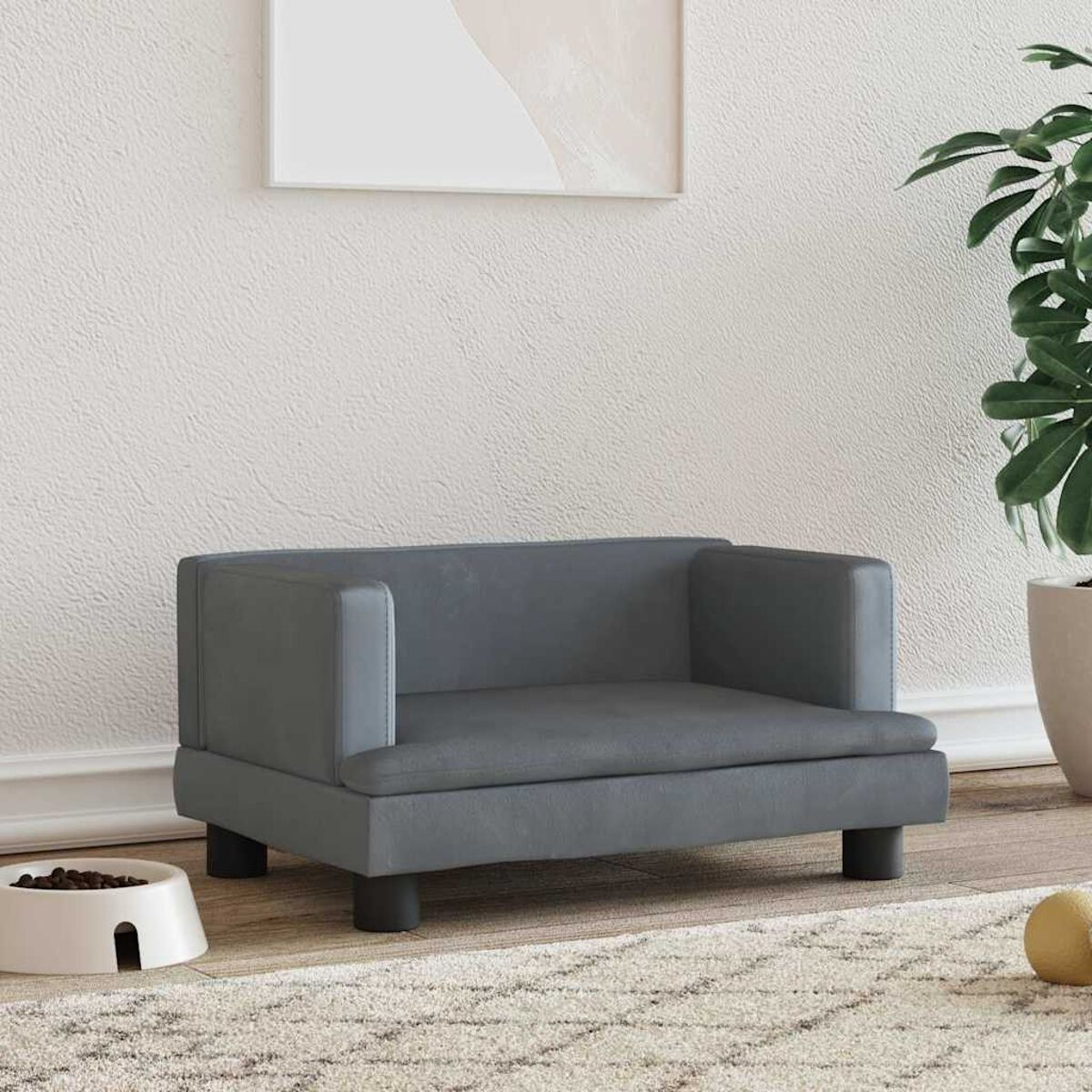 Ein graues Haustiersofa mit schwarzen Beinen. Eine Futterschüssel, ein Ball und eine Pflanze im Vorder- und Hintergrund.