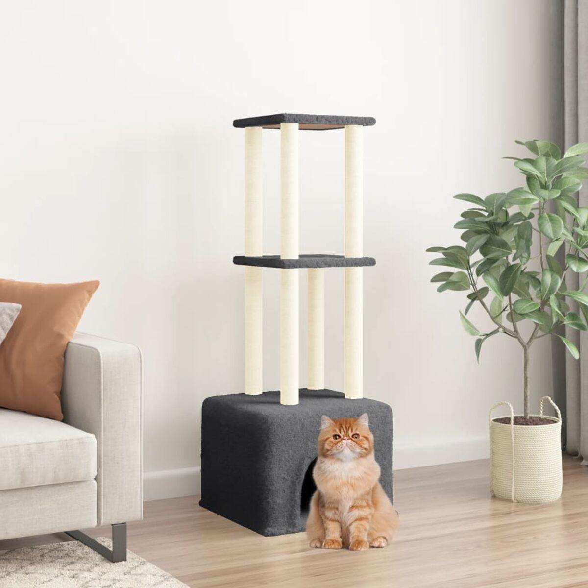 Katze sitzt in einem grauen Kratzbaum. Zimmerpflanze und Couch im Hintergrund.