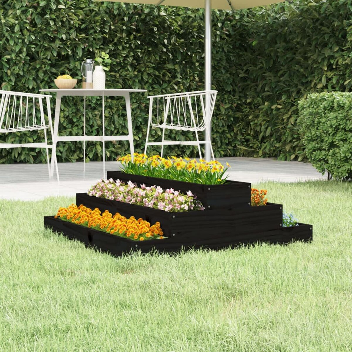 Mehrstufiges schwarzes Blumenbeet mit bunten Blumen. Ein Tisch und Stühle sind im Hintergrund.