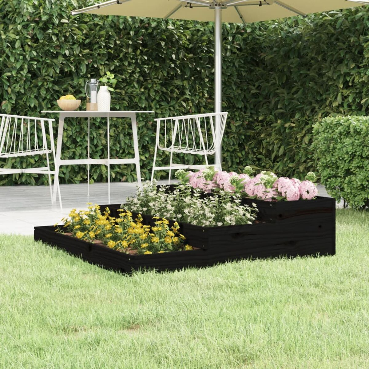 Ein schwarzes Hochbeet mit Blumen auf einem grünen Rasen, im Hintergrund ein weißer Tisch.