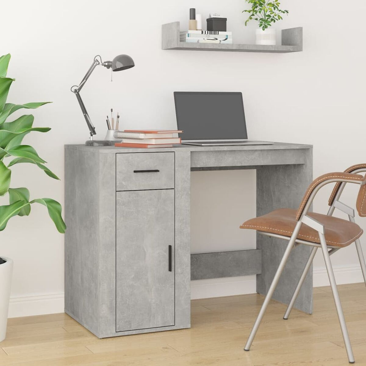 Grauer Schreibtisch mit Laptop, Lampe und Stuhl. Links steht eine Pflanze. Oben ist ein Regal.