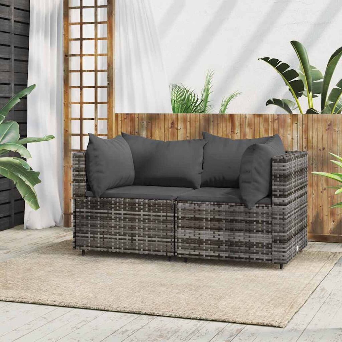Gewebenes Outdoor-Sofa mit Kissen, auf beigem Teppich, mit natürlichem Hintergrund.