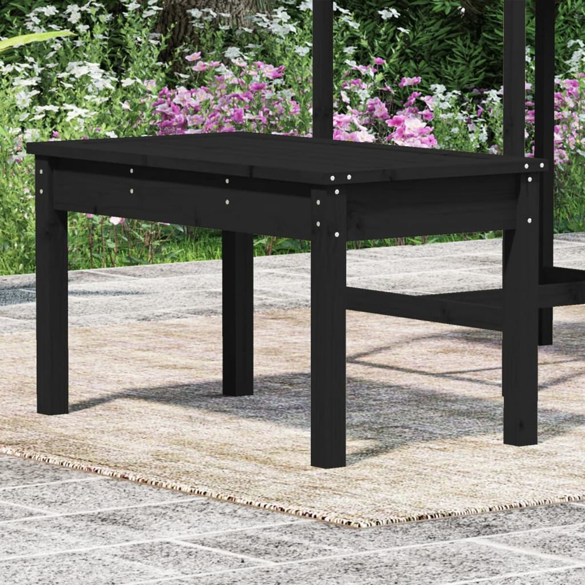 Ein schwarzer Tisch auf einer Terrasse, mit verschwommenem Hintergrund aus Grün und Sitzbereich.