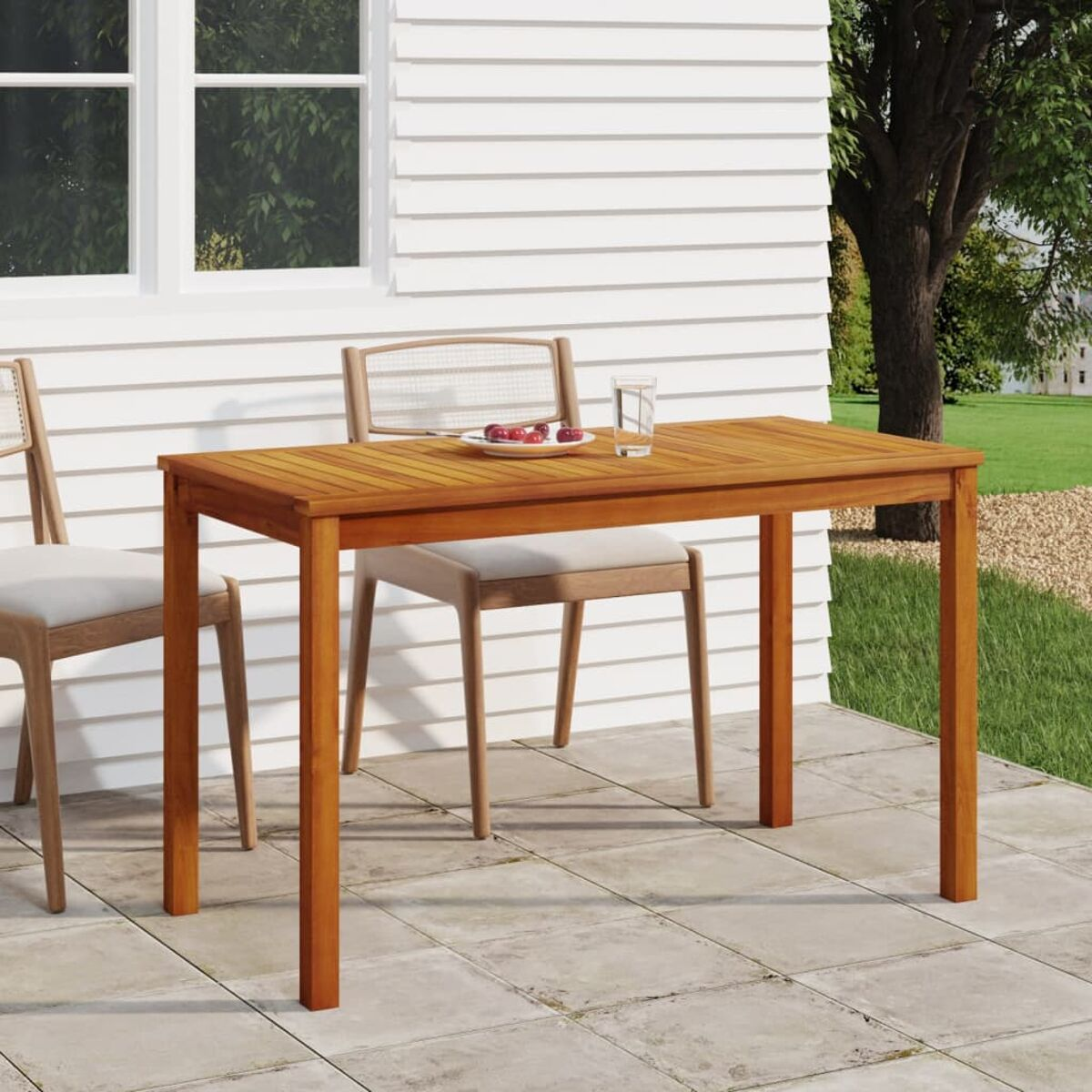 Holztisch mit Essen und Glas. Zwei Stühle stehen neben dem Tisch. Im Hintergrund ist ein weißes Gebäude.