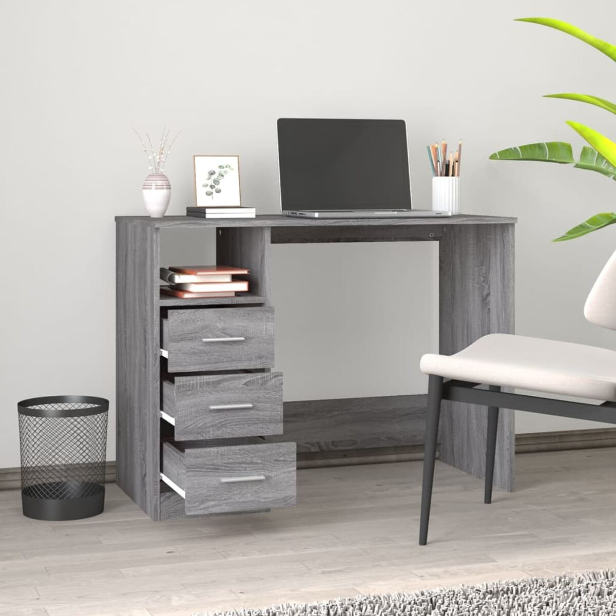 Grauer Schreibtisch mit Schubladen, Laptop, Büchern und Mülleimer. Hintergrund: weiße Wand.