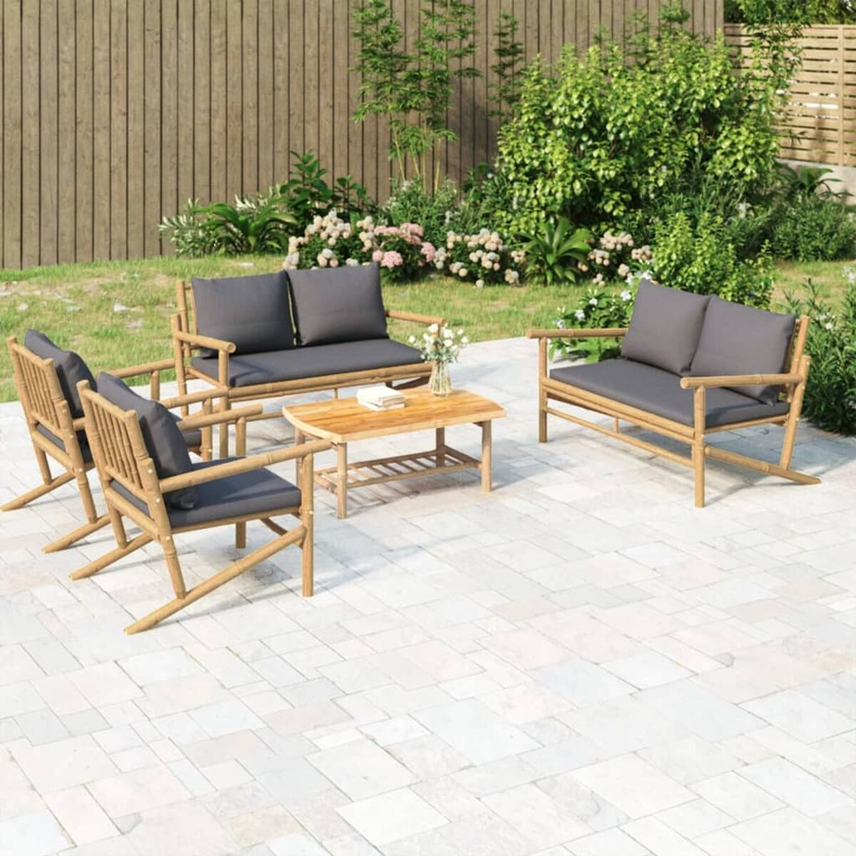 Gartenmöbel-Set aus Bambus in einem Garten. Enthält Stühle, ein Sofa und einen Tisch.