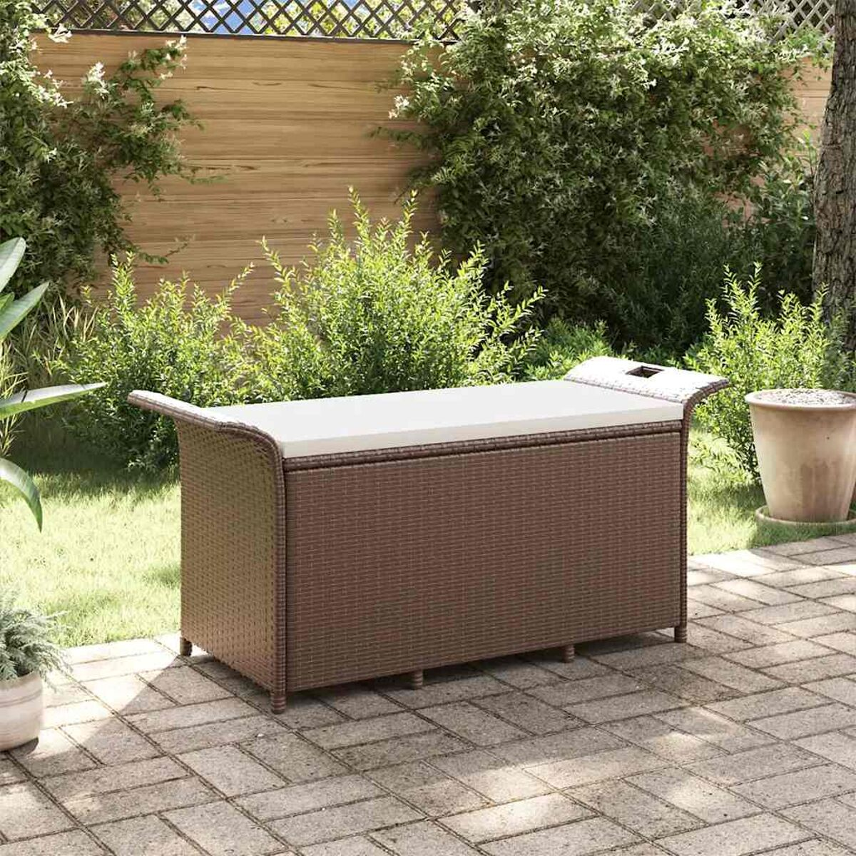 Outdoor-Aufbewahrungsbox aus Korbgeflecht mit gepolsterter Oberseite. Auf einer Ziegelterrasse. Grüne Pflanzen im Hintergrund.