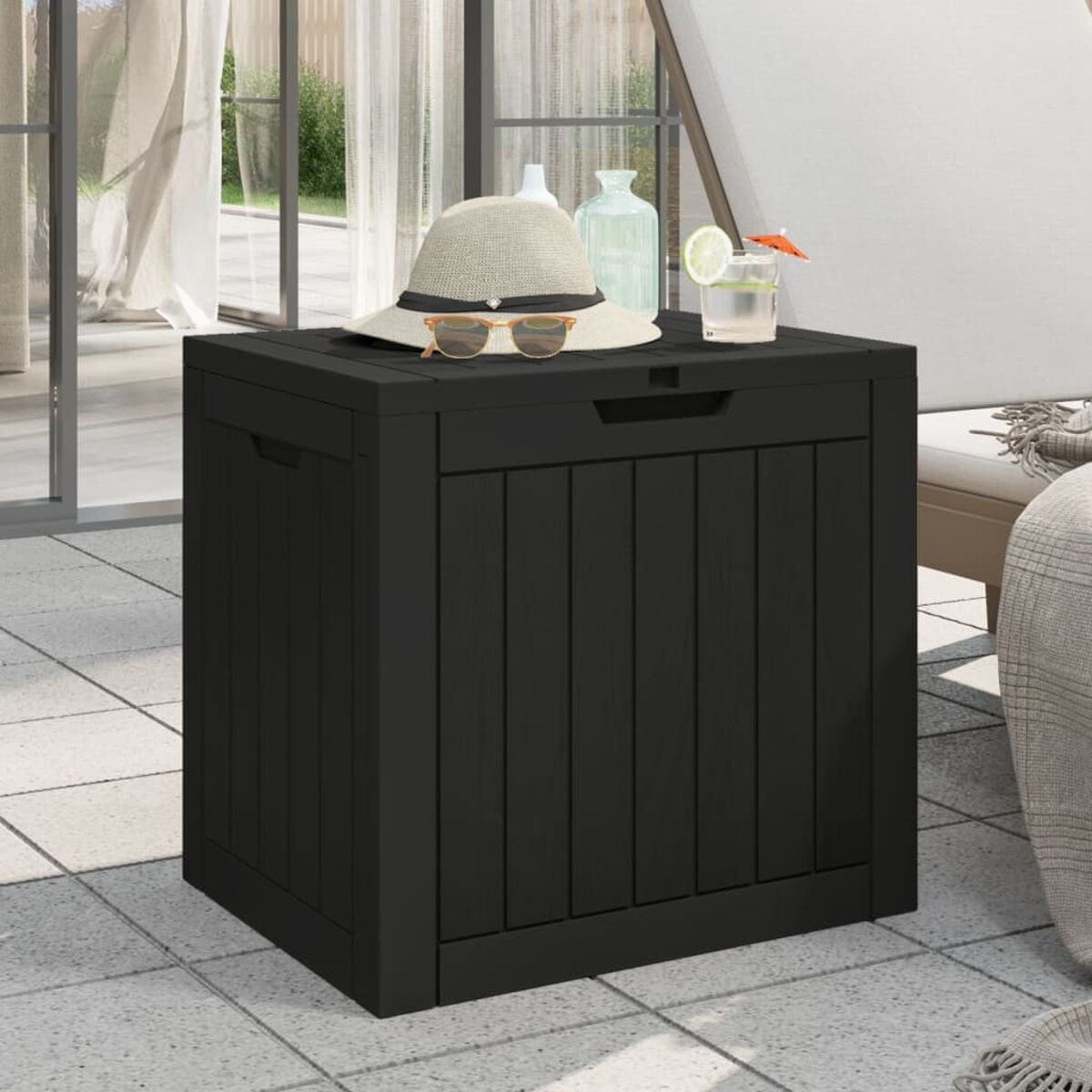Schwarze Outdoor-Aufbewahrungsbox mit Hut, Sonnenbrille und Getränk darauf, auf einer Terrasse.