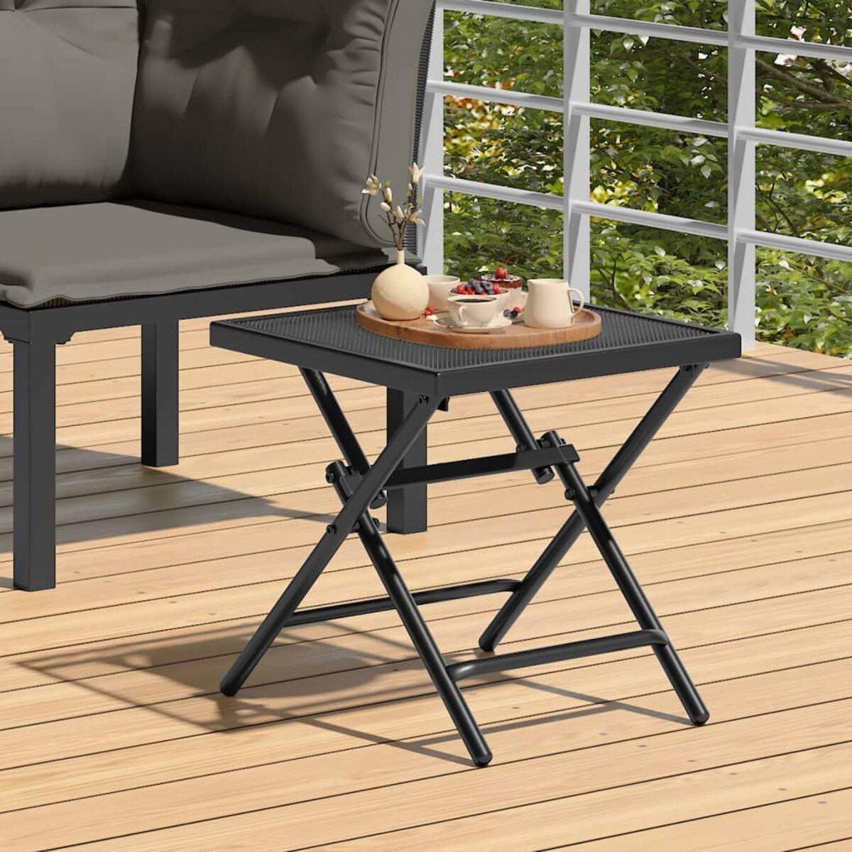 Schwarzer Klapptisch auf Holzterrasse mit Gegenständen und einem Stuhl in der Nähe.