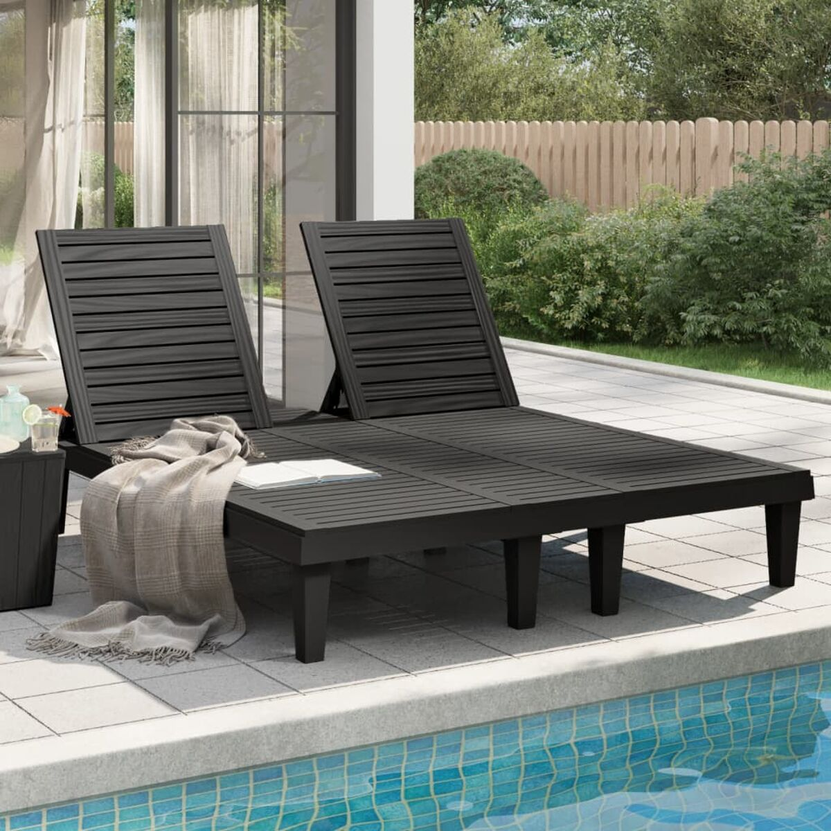 Zwei schwarze Liegestühle und ein kleiner Tisch an einem Pool. Eine Decke und ein Getränk sichtbar.