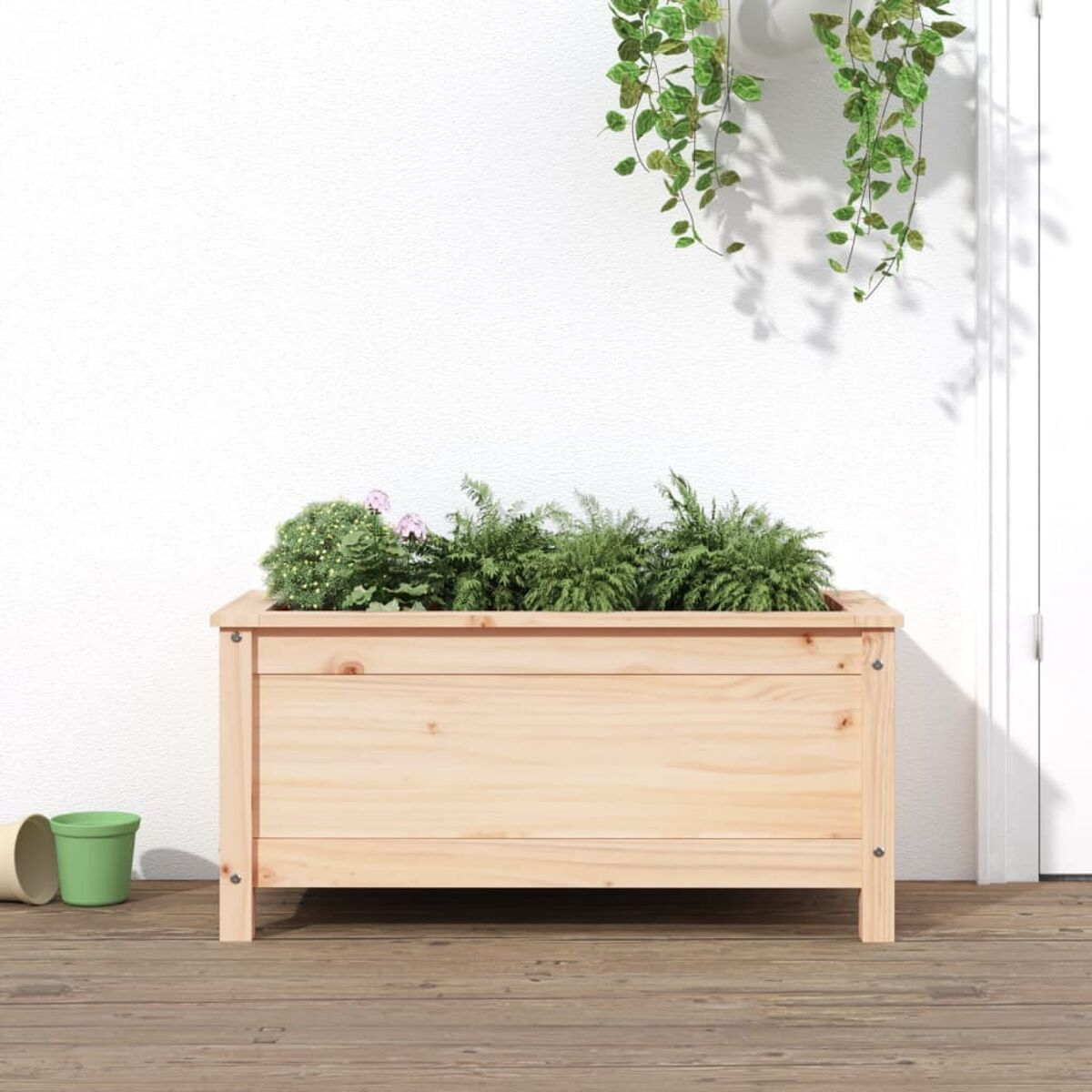 Hölzerner Pflanzkasten mit Pflanzen auf einem Holzdeck. Weiße Wand und grüne Blätter im Hintergrund.