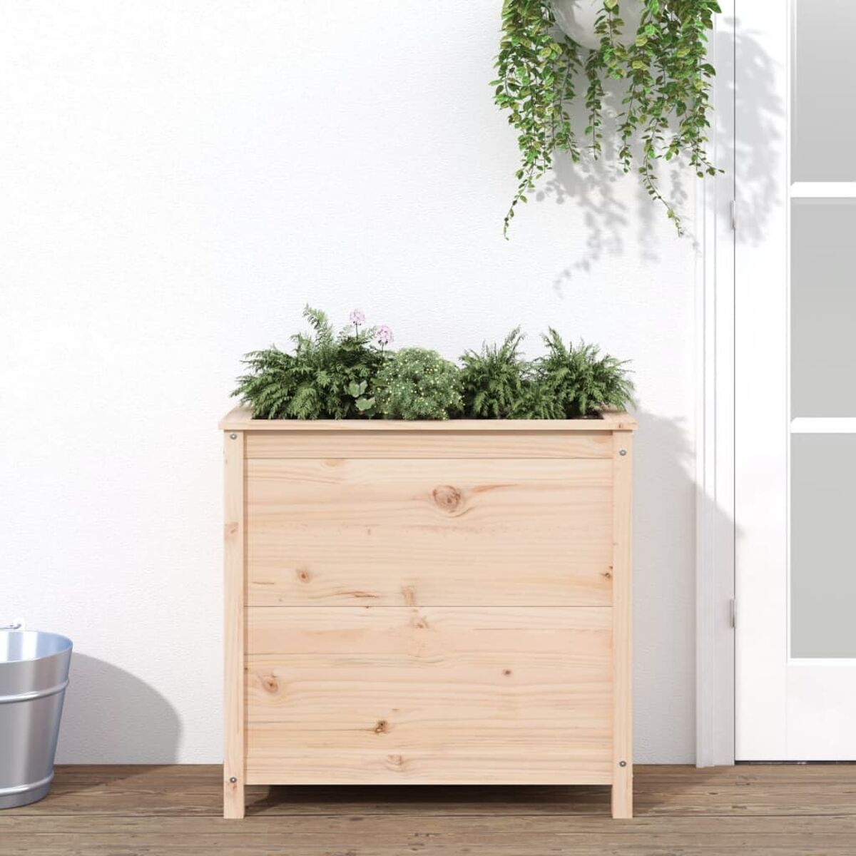 Holzpflanzkasten mit Pflanzen gefüllt. Er steht auf einer Holzterrasse, mit weißer Wand und Hängepflanzen.
