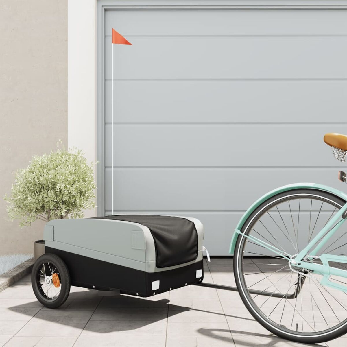Fahrrad zieht Anhänger mit Fahne, geparkt vor Garage.