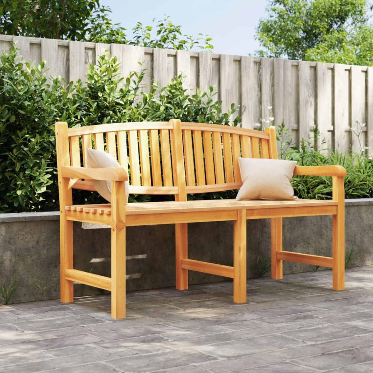 Holzbank mit gebogener Rückenlehne und zwei beigen Kissen. Sie steht auf einer Backstein-Terrasse.