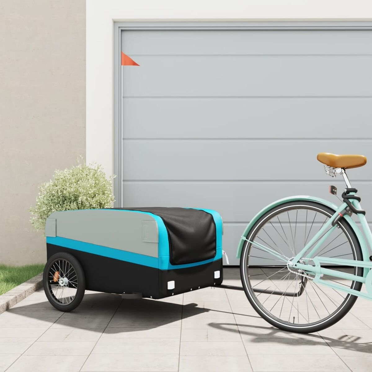 Ein türkisblaues Fahrrad mit Anhänger, geparkt in der Nähe einer Garage. Rote Flagge am Anhänger.