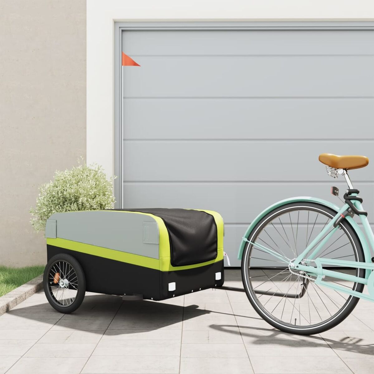 Fahrradanhänger, der von einem Fahrrad vor einer Garage gezogen wird. Anhänger ist grau, schwarz und gelb. Grüne Pflanzen.