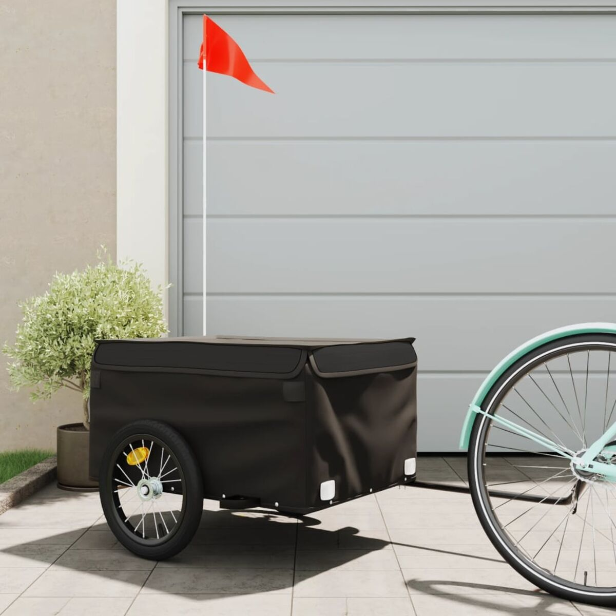 Schwarzer Fahrradanhänger mit roter Fahne, geparkt in der Nähe einer Garage und eines Fahrrads.