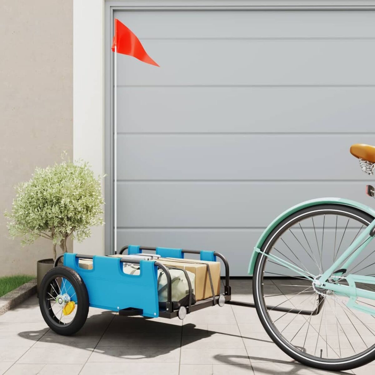 Blauer Fahrradanhänger mit roter Flagge, an einem Fahrrad. Geparkt vor einer Garage.