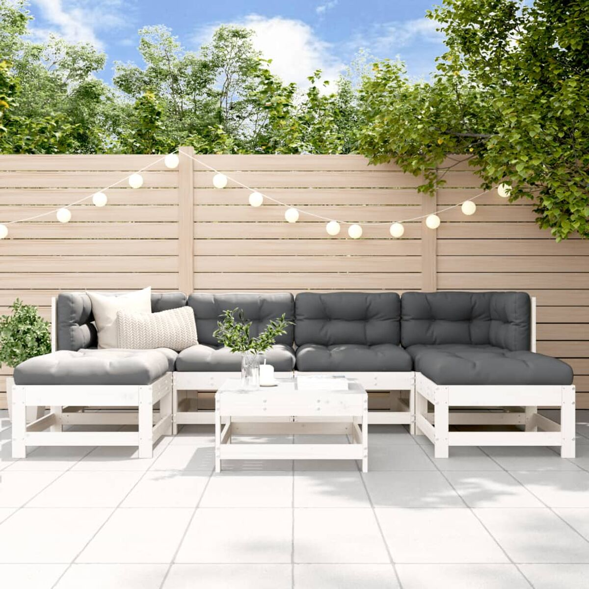 Weißes Holz-Outdoor-Sofa mit grauen Kissen. Tisch und Lichter im Hintergrund.