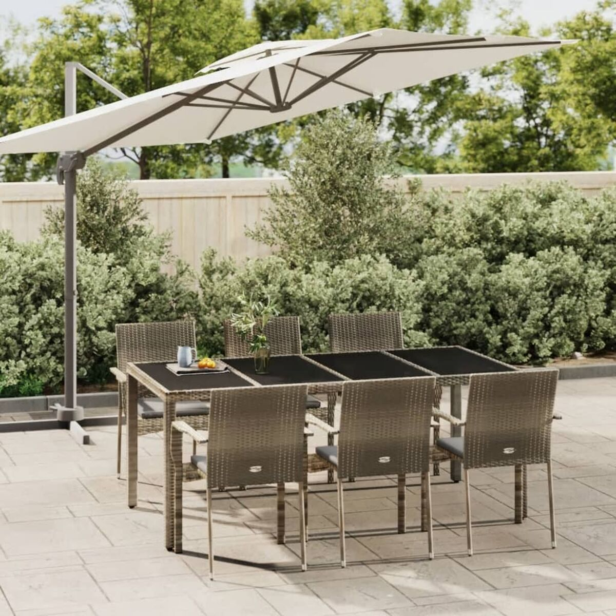 Ein Terrassenset mit Tisch, Stühlen und Sonnenschirm. Der Hintergrund umfasst Bäume und einen Zaun.