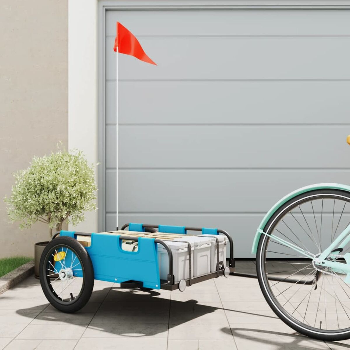 Ein Fahrrad mit blauem Anhänger und roter Fahne vor einem Garagentor.