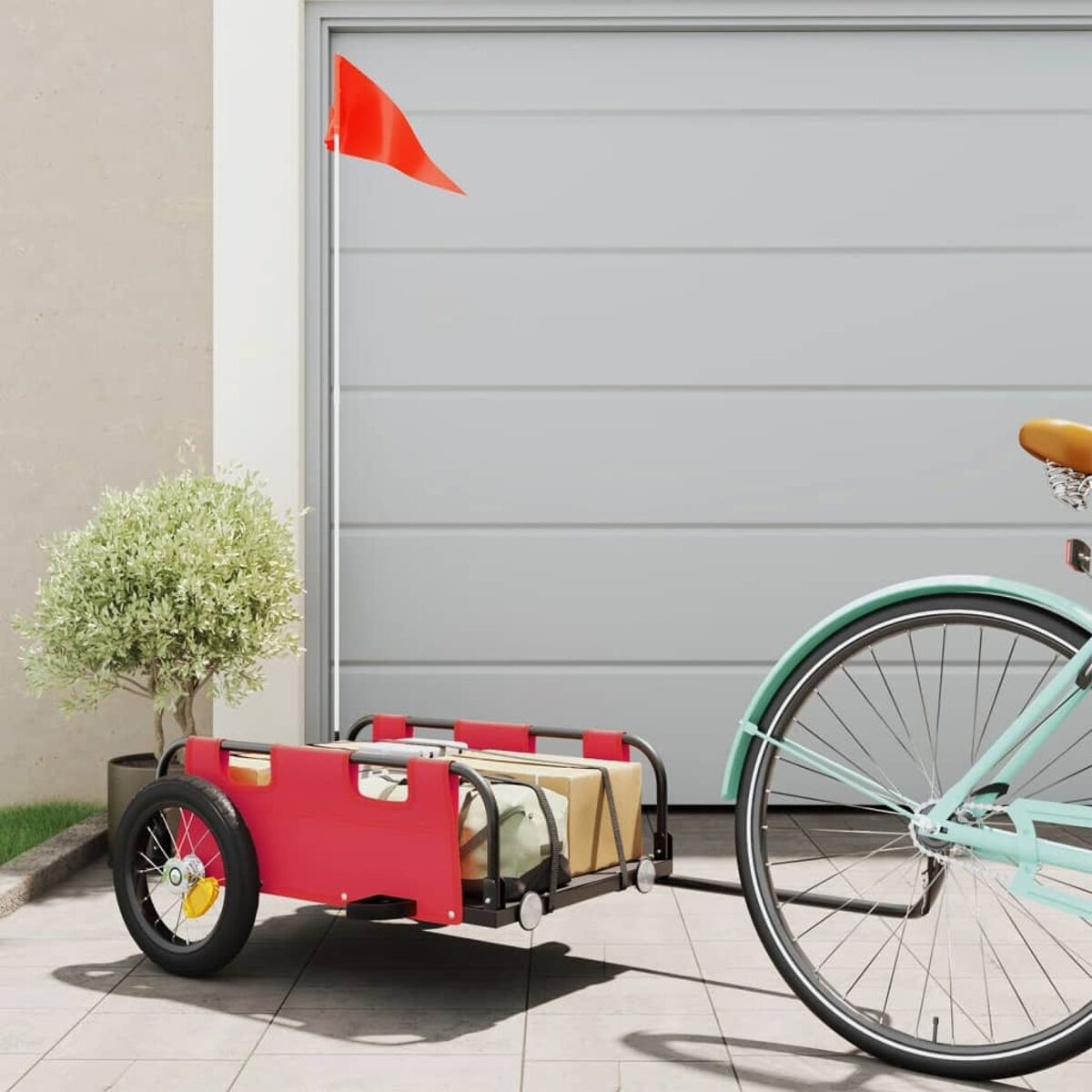 Ein roter Anhänger mit roter Fahne an einem Fahrrad, geparkt vor einem grauen Garagentor.