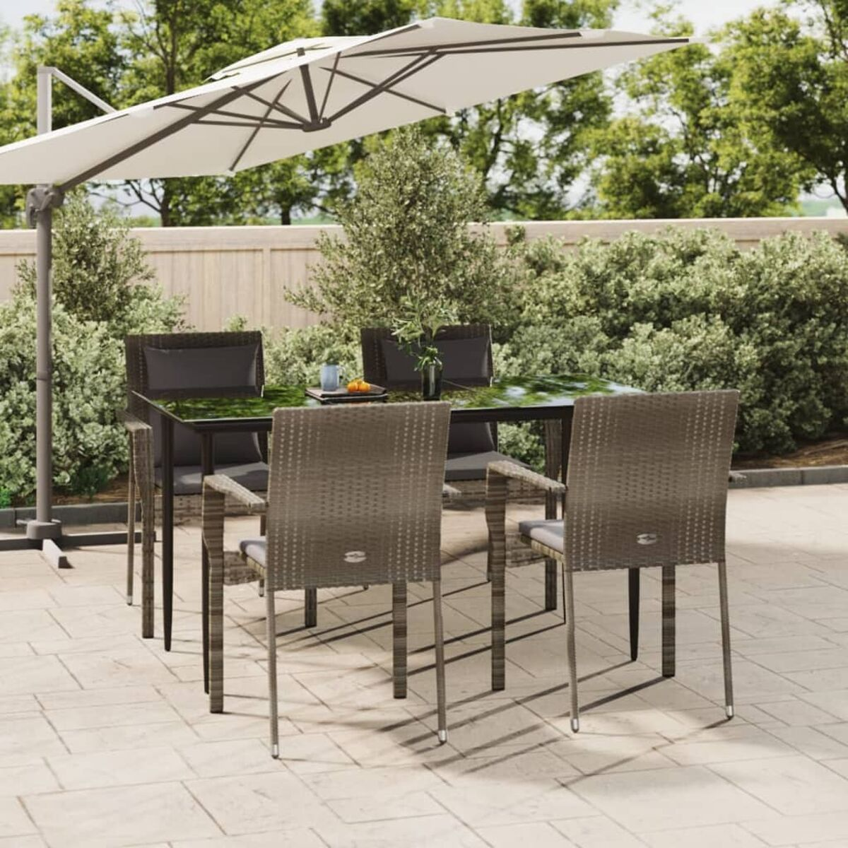 Terrassenset: Tisch, vier Stühle, großer Schirm und üppiges Grün.