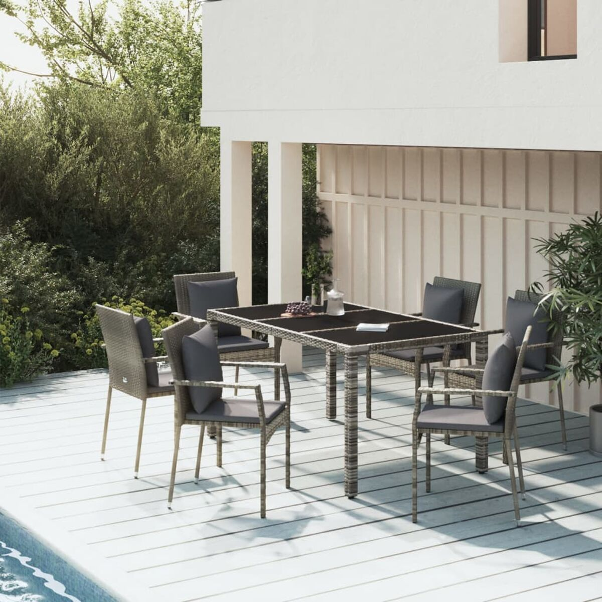 Essgruppe im Freien mit Tisch und Stühlen in der Nähe eines Pools. Der Tisch ist gedeckt, Gebäude weiß.