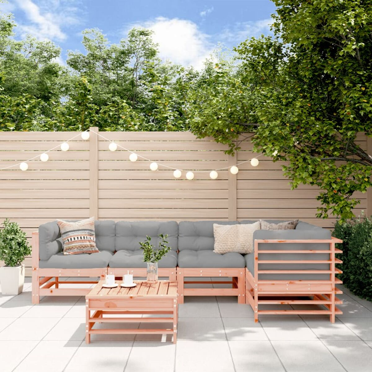 Terrassenmöbel mit hellgrauen Kissen. Grüne Bäume und Zaun im Hintergrund.