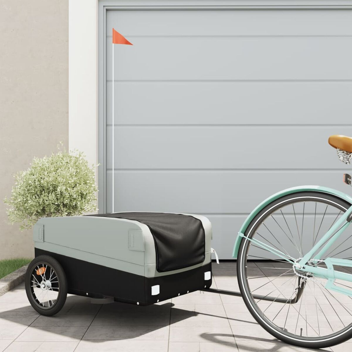 Ein Fahrradanhänger mit schwarzem Container und Fahne, geparkt vor einer Garage.