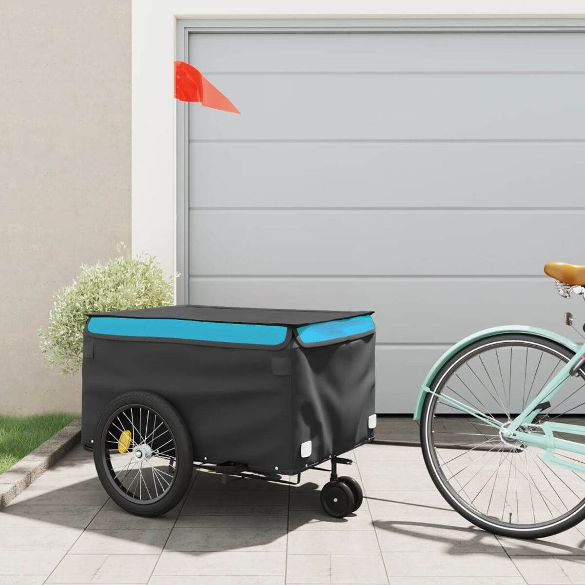 Schwarzer und blauer Fahrradanhänger neben einem mintfarbenen Fahrrad. Garage und rote Fahne im Hintergrund.