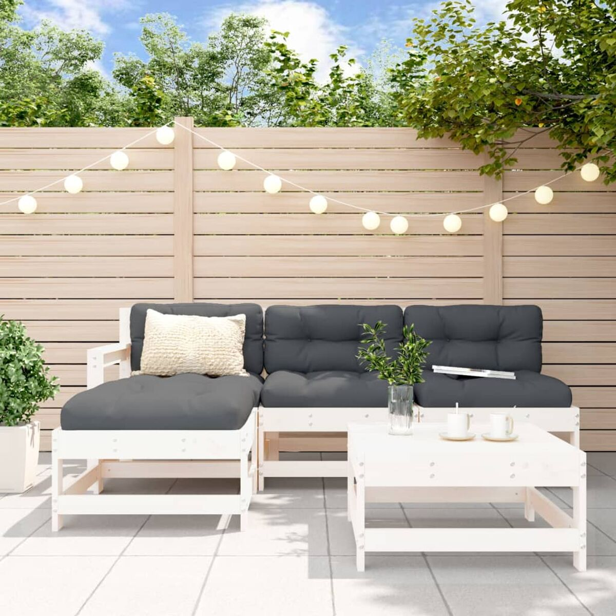Garten-Terrassenset mit weißem Rahmen, grauen Kissen und einem Couchtisch. Ein Holzzaun und Grünzeug sind im Hintergrund.